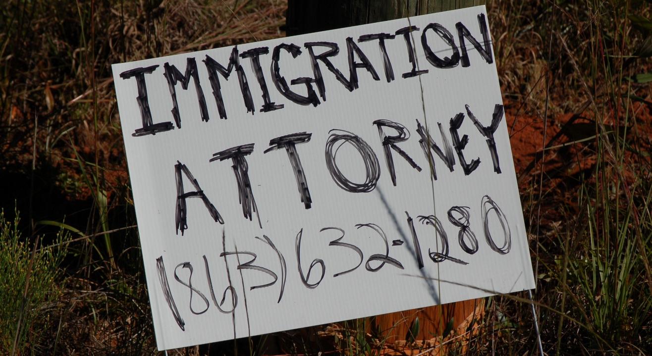 Photograph of a roadside sign advertising the telephone number of an immigration attorney.