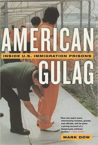 Cover of the book American Gulag by Mark Dow. The image shows a group of men in orange jumpsuits at an immigration detention facility. They are standing in front of a chain link fence and being patted down by uniformed officers. 